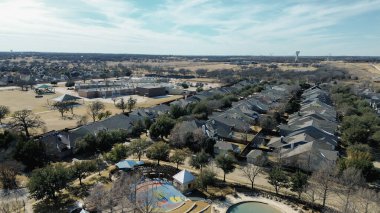 Lantana Patikası yakınlarındaki okul kompleksinde renkli çocuk parkı ve açık spor sahalarının yanında dairesel havuz. Parlak gölgeler, kış çayırları, yumuşak gölgeler, değişik çatı, kış manzarası, Lantana, Texas. ABD