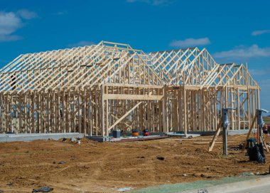 Duvar çivileri ve çatı kirişleri birincil yapı yapısını oluştururken, araç kutuları ve kaldırım işaretleri de çok önü tanımlıyor. Güneşli kereste, yumuşak toprak hatları, sessiz banliyö tonları, Aubrey, Teksas. ABD