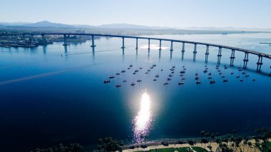 Demir atmış körfez koridoru, San Diego Körfezi üzerinde yükselen Coronado Köprüsü 'nü, demirlemiş yelkenli tekneleri ve Tidelands Parkı' nın yakınında palmiye çizgili kıyı şeridi ile yakalıyor. Yansıtıcı su, yumuşak kıyı dokuları, CA. ABD
