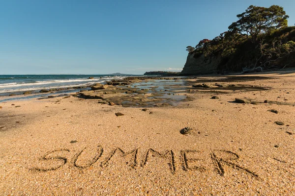 Nieuw-Zeeland strand met woord zomer geschreven in zand — Stockfoto