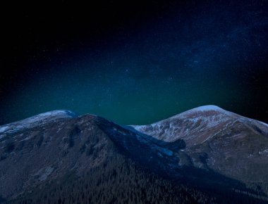 Kısmen karla kaplı dağların tepesindeki yıldızlı gökyüzü. Resimli gece manzarası.