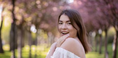 Parktaki sokakta gülümseyen beyaz elbiseli çekici esmer. Portre