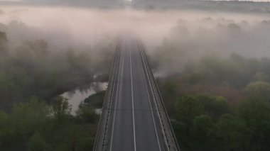 Sisli bir çayır ve şafakta bir yol köprüsü. Resimli yaz sabahı manzarası. Hava görünümü.