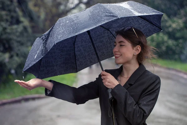 Atractiva morena bajo un paraguas atrapa gotas de lluvia. —  Fotos de Stock