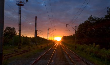 Gün batımında ya da şafakta demiryolu. Seyahat konsepti. Koyu mavi fırtına bulutları, kavurucu güneş ve tren platformunun yanında karanlık bir orman..