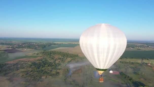 Ένα μεγάλο άσπρο μπαλόνι πετάει πάνω από την ύπαιθρο την αυγή. — Αρχείο Βίντεο