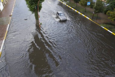 Kenar mahallelerde meydana gelen anormal bir sağanak sonrası sokakları su bastı. Su basmış caddede arabalar hareket ediyor. Doğal bir felaketin sonuçları..