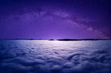 Bulutların ya da sislerin üzerinde yıldızlı gökyüzü. İnsansız hava aracının görüntüsü. Mistik ya da büyülü bir atmosfer.