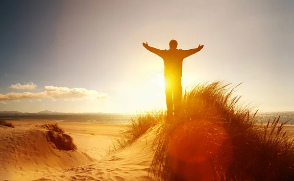 Gün batımında bir adamın silueti. Gün batımında genç adam ellerini kaldırır.