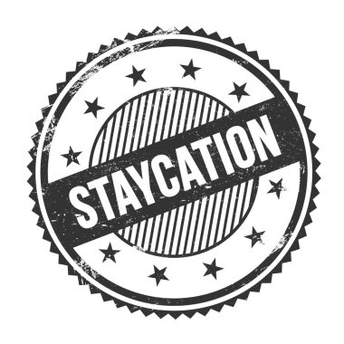 STAYCATION metni siyah grungy zig zag kenarları yuvarlak pul üzerine yazılmış.