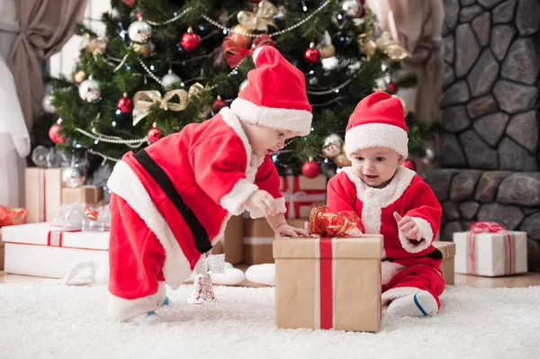 Noel ağacında hediyelerle Noel Baba gibi giyinmiş çocuklar.