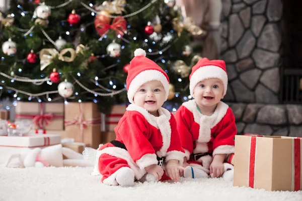 Noel ağacında hediyelerle Noel Baba gibi giyinmiş çocuklar.
