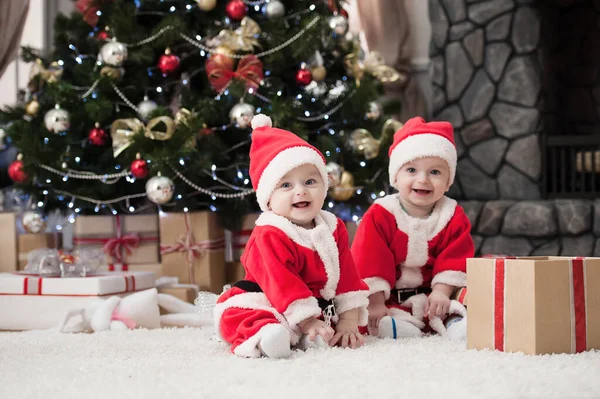 Noel ağacında hediyelerle Noel Baba gibi giyinmiş çocuklar.