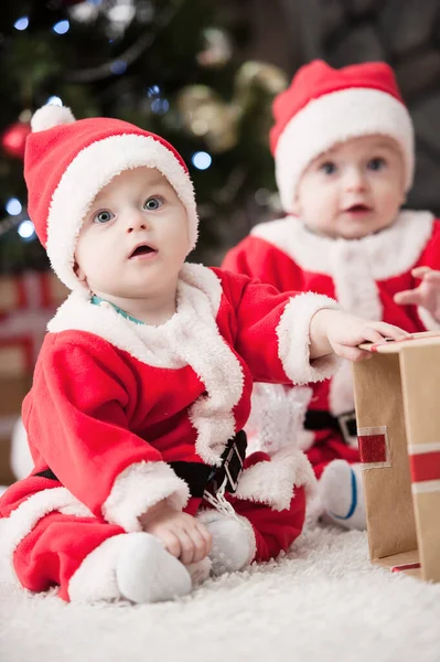 Noel ağacında hediyelerle Noel Baba gibi giyinmiş çocuklar.