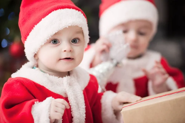 Noel ağacında hediyelerle Noel Baba gibi giyinmiş çocuklar.