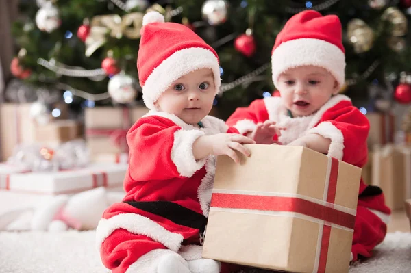 Noel ağacında hediyelerle Noel Baba gibi giyinmiş çocuklar.