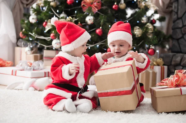 Noel ağacında hediyelerle Noel Baba gibi giyinmiş çocuklar.