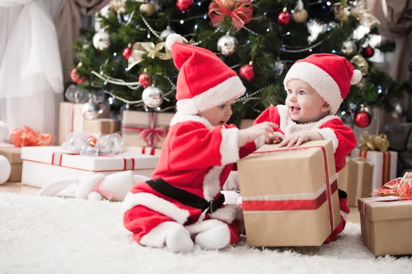 Noel ağacında hediyelerle Noel Baba gibi giyinmiş çocuklar.