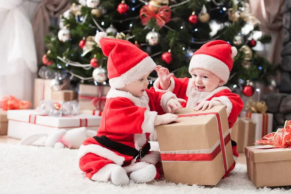 Noel ağacında hediyelerle Noel Baba gibi giyinmiş çocuklar.