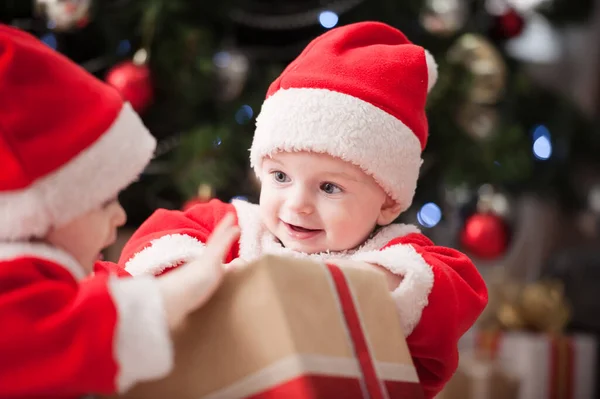Noel ağacında hediyelerle Noel Baba gibi giyinmiş çocuklar.