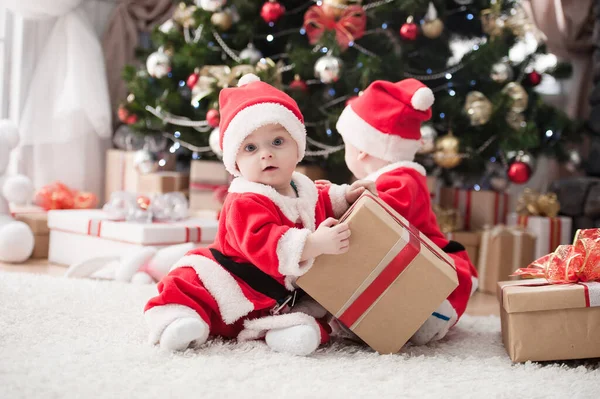 Noel ağacında hediyelerle Noel Baba gibi giyinmiş çocuklar.