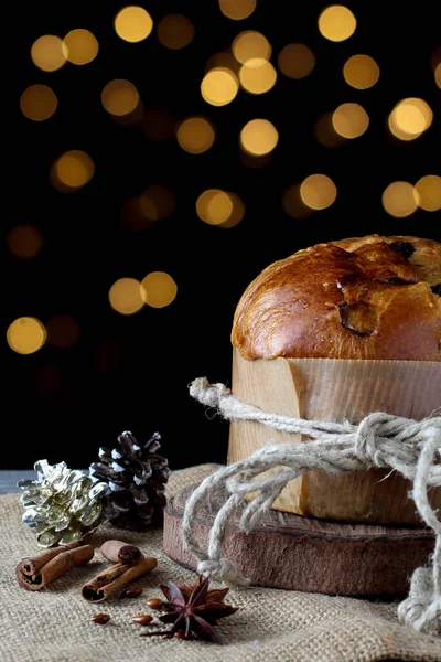Panettone kuru üzümlü, jüt kumaşlı sol tarafta Noel süslemeleri ve arka planda bir sürü ışık var.