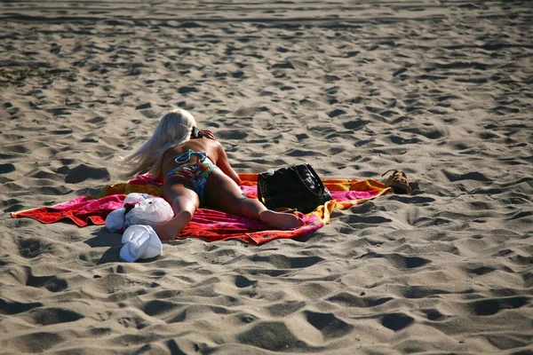 Eine junge blonde Frau am Telefon, die im Sand liegt — Stockfoto