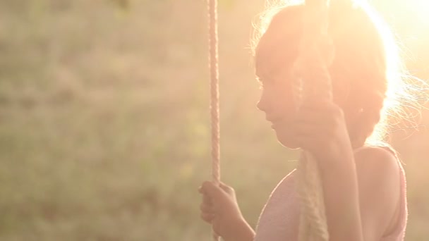 A menina treme em um balanço em um pôr-do-sol — Vídeo de Stock