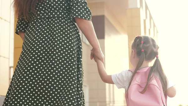 Little daughter schoolgirl walks with a backpack and holds her mothers hand. preschool education concept. happy family mother and child go to school holding hands. — Stock Photo, Image
