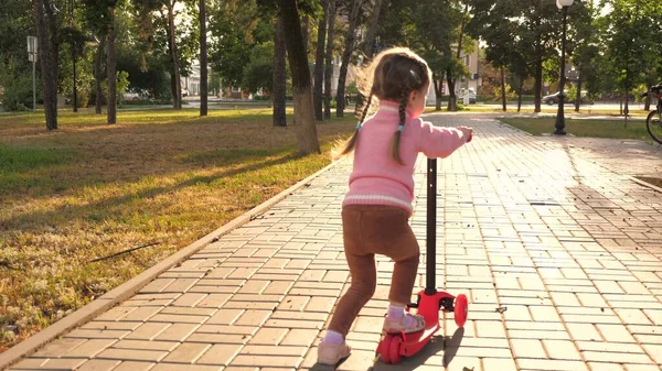 A menina aprende a andar de scooter. menina feliz brincando no parque. criança saudável monta uma scooter na cidade na rua. conceito de infância feliz — Fotografia de Stock