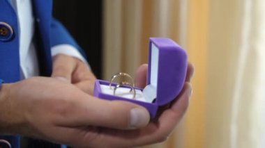 Adam alyansları elinde tutuyor. Damat mavi takım elbiseli ve beyaz gömlekli güzel bir kutuda altın yüzüğünü tutuyor. Sevdiğin kadın için değerli bir hediye.