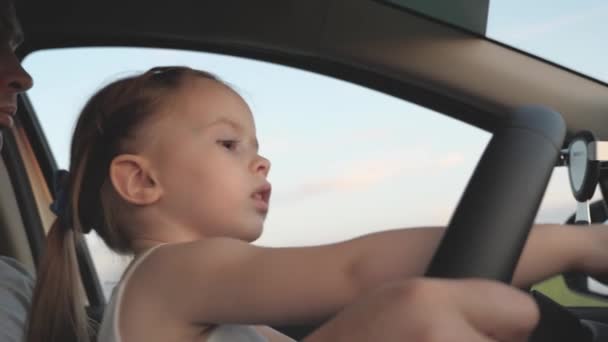 Malá zdravá dcera řídí auto, které otáčelo volantem na tátově klíně. Otec cestuje s dětmi autem. Řidič a ten kluk řídí. šťastný rodinný a dětský koncept — Stock video