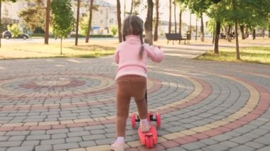 Küçük kız scooter sürmeyi öğreniyor. Parkta oynayan mutlu bir kız bebek. Sağlıklı bir çocuk sokakta scooter 'a biniyor. Mutlu çocukluk kavramı