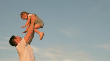 Babam mavi gökyüzüne mutlu bir kız çocuğu fırlatıyor. Mutlu aile yolculukları. Baba ve küçük sağlıklı çocuk birlikte oynar, güler ve sarılırlar. Bebeğin ebeveynin kollarında. Baba izinli. Mutlu aile kavramı.