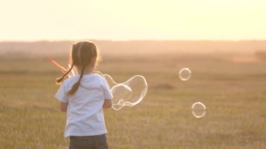 Küçük bir kız gün batımında büyük kabarcıklar çıkarıyor. Küçük bir çocuğun çocukluğu. Parktaki çocuk oyunu