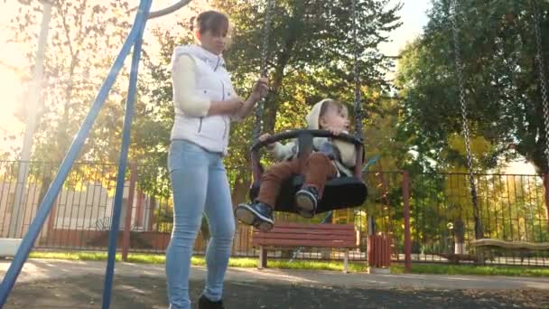 Bonne famille maman roule le petit enfant en vol sur balançoire dans le parc. Le week-end, mère et fille marchent. Promenades en famille dans le parc. Enfant et jeune parent. concept d'enfants et de famille. Travail d'équipe — Video