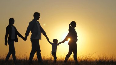 Mutlu yedinin silueti, el ele yürüyor, gün batımında tarlada yürüyor. Çocuklar anne ve babalarının elini tutuyor. Mutlu küçük çocuk ve ebeveynler güzel güneş ışınlarında yürürler, tatile çıkarlar. a