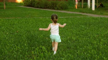 Mutlu çocuk yazın yeşil bir çimenlikte çayırda koşar. Neşeli küçük kız sahada koşuyor. Mutluluk kavramı. Çocuk yazın çimenlerde oynuyor. Ağır çekim. Bebek baharda parkta oynuyor..