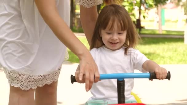 Mama uczy dziecko jeździć na rowerze w letnim zielonym parku. Szczęśliwe dziecko bawi się z matką. Rodzic bawi się ze śmiejącą się córką. Praca zespołowa. Zbliżenie — Wideo stockowe