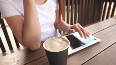 Yazlık kafede bir kız tablet kullanır ve lezzetli aromatik kahve içer. Kadın sohbeti, kahve içmesi ve dinlenmesi. Kafedeki genç kadın bir aletle çalışıyor..
