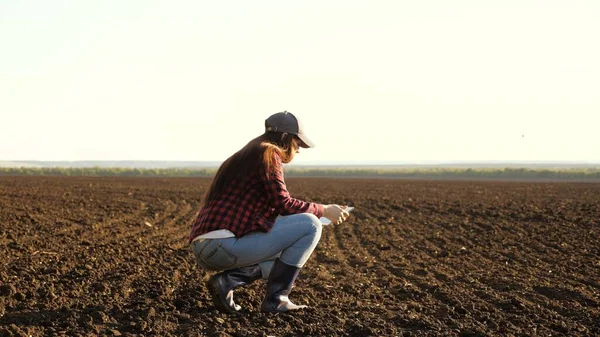 Un agriculteur vérifie la qualité du sol avant de semer. agricultrice avec une tablette dans les champs tient la terre dans ses mains. girl agronome vérifie la qualité du grain de semis. femme d'affaires vérifie son domaine — Photo