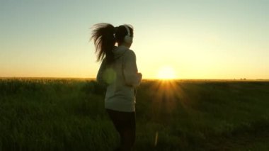 Genç Atletizm Kadını Yolda Hızlı Koşarken, Sıkı Antrenman Yaparken, Yarış Yarışması veya Maraton İçin Hazırlanırken. Siyah spor kıyafetli kız Şafakta Yeşil Tarlalar boyunca koşuyor.