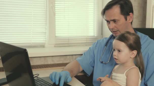 Concept d'examen pédiatrique pour le traitement des enfants. Médecin pédiatre professionnel attentionné, jouant avec un enfant préscolaire mignon et travaillant sur un ordinateur portable. fille patient assis sur les genoux du pédiatre — Video