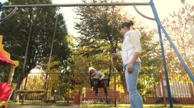 Mutlu aile annesi küçük çocuğu parkta salıncakta sallıyor. Hafta sonları, anne kız yürürler. Aile parkta yürüyor. Çocuk ve genç ebeveyn. Çocuklar ve aile kavramı. Takım çalışması.