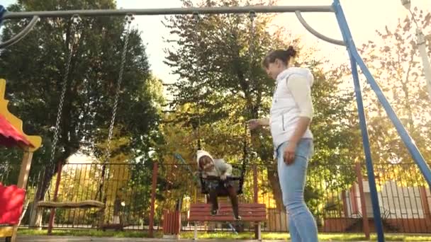 Happy family mom rolls the little child in flight on swing in the park. On weekends, mother and daughter walk. Family walks in park. Kid and young parent. concept of children and family. Teamwork — Stock Video