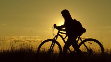 Kadın bisikletçi bir engeli aşar. Sağlıklı genç bayan turist bisikletle yamaçtan aşağı iniyor, doğanın tadını çıkarıyor, temiz hava alıyor. Özgür bir kız gün batımında bisikletle seyahat eder. macera ve seyahat kavramı.