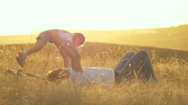 Baba küçük kızıyla parkta battaniyenin üzerinde oynuyor. Babası çocuğu elleriyle fırlatıyor, çocuk mutlu ve gülüyor. Mutlu baba ve küçük çocuk güneşin altında doğada sarılırlar. Aile tatilde..