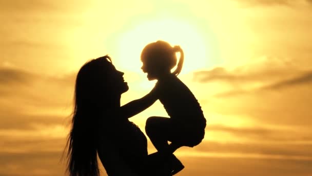 Mom is holding her beloved healthy daughter in her arms. happy family mother and little child are screaming in park in nature in the sun. silhouette of mom and baby at sunset. cheerful childhood — Stock Video