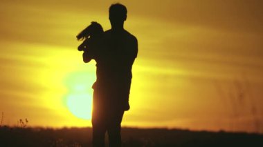 Baba ve küçük kızı birlikte oynuyorlar. Baba, sevgili kızının etrafında güneş ışınlarıyla dönüyor. Mutlu aile, gün batımında tarlada baba ve kız. Mutlu aile ve sağlıklı çocukluk kavramı.