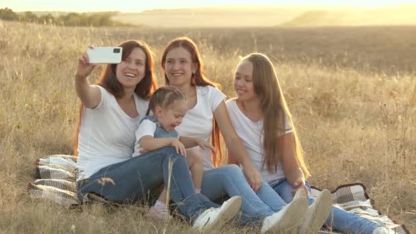 Lyckliga familjeresor, selfie på smartphone i parken. Mamma och friska barn sitter på en filt. Mamma med sina döttrar fotograferas i fält på filt. familjeresor och äventyr — Stockvideo